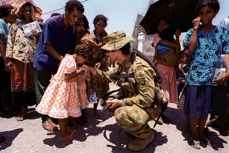 Image: Defence Australia |  Sergeant Martin Ryan shakes hand with a young girl in front of the half-constructed church where the Suai massacre began.