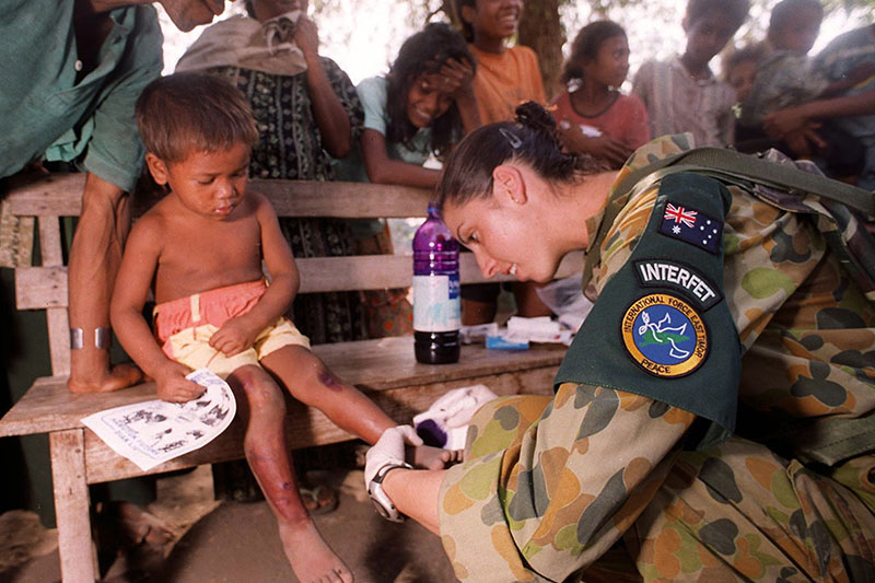 Image: Defence Australia | Private Tammy Smithson, a Medical Assistant from 3rd Brigade tends to a small child in the devastated town of Suai.
