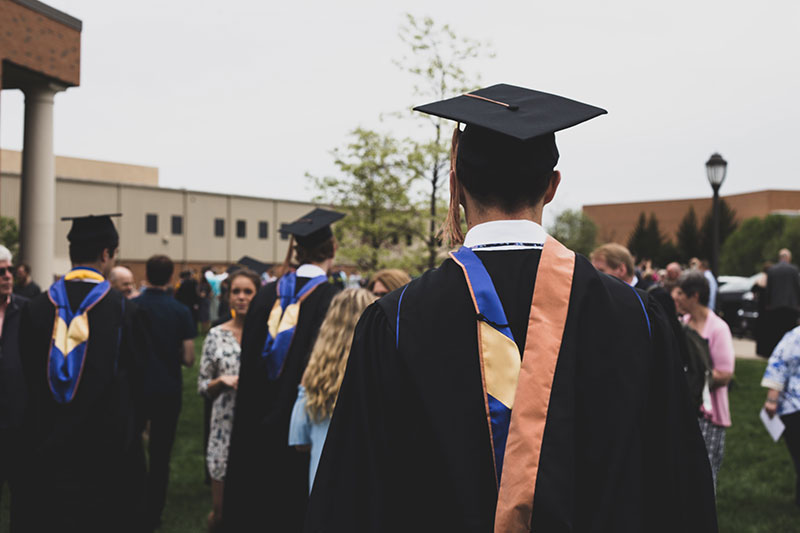 Student walking through a ground wearing graduation clothing. 